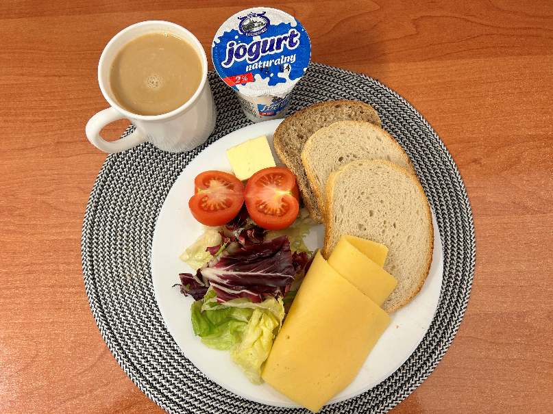 Na zdjęciu znajduje się: Jogurt naturalny, Kawa zbożowa z mlekiem, Chleb mieszany pszenno-żytni, Chleb Graham, Masło extra 82%, Ser żółty, Pomidor, Mix sałat